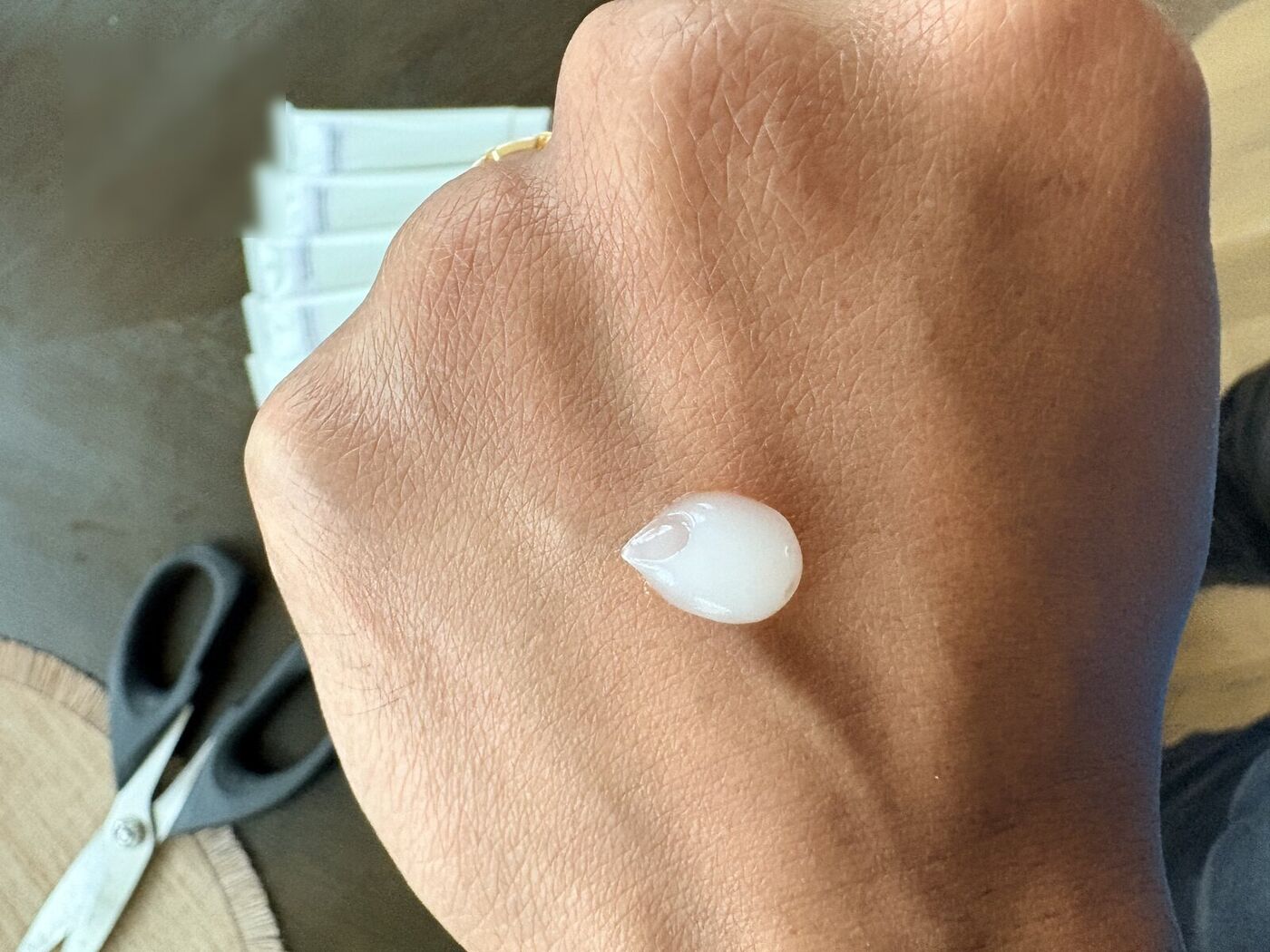 A small dollop of white sunscreen on the back of a hand, with sample tubes softly out of focus in the background.