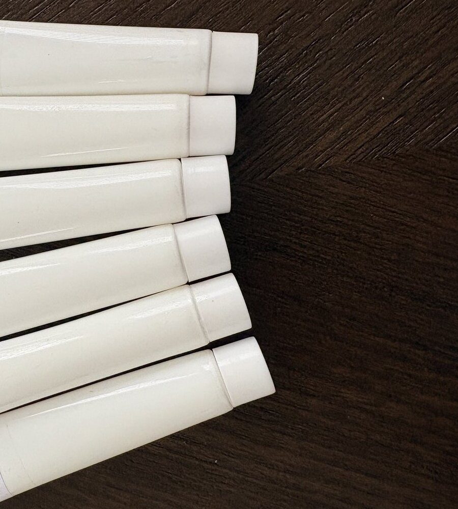 Six identical white sunscreen tubes fanned out on a dark wood surface, photographed from the cap end.